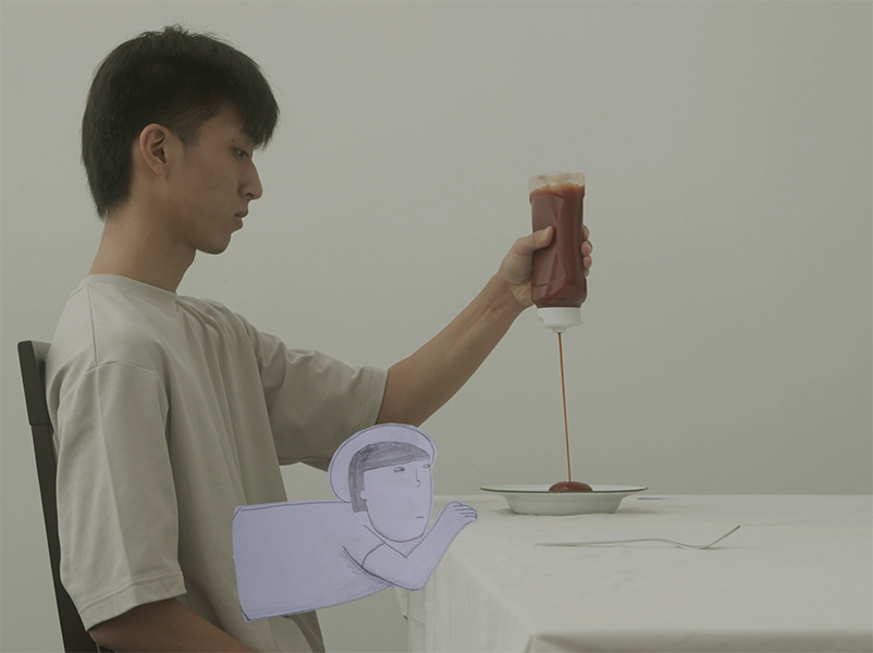 A man in a cream t-shirt squeezes a bottle of ketchup onto his plate in a empty room save for a table. A small man with a hat who appears as a paper cut-out protruding from his stomach stares critically at the plate.