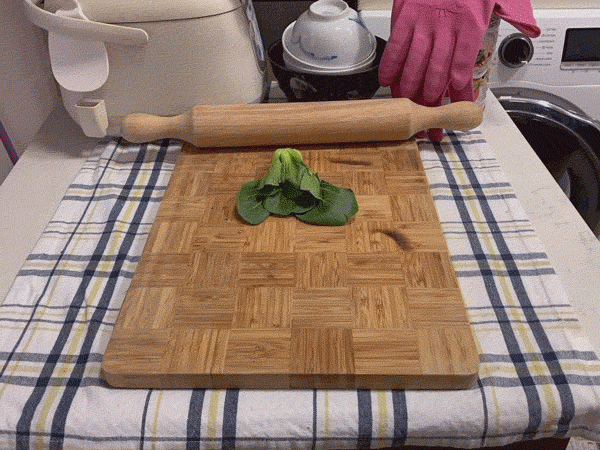 A replacement animation of a naibai vegetable being rolled out into a spring onion by a rolling pin, on a chopping board, in a kitchen